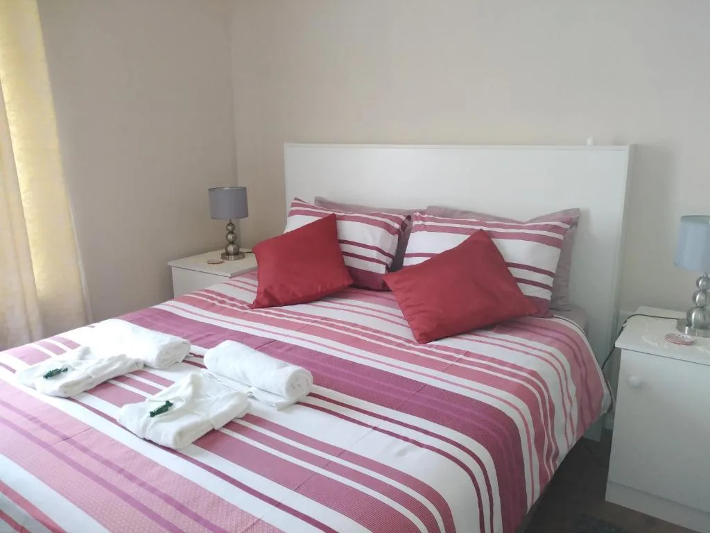 Bedroom with striped pink bedding, red cushions, and rolled towels on bed