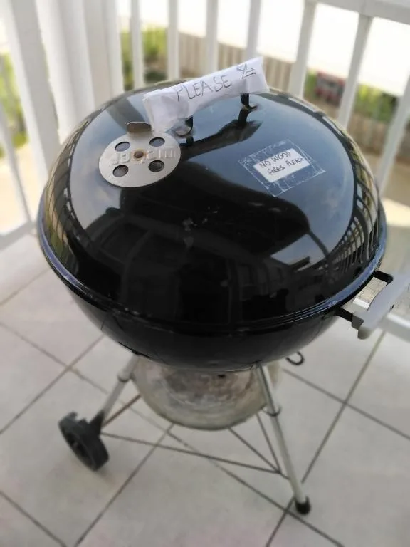 Black kettle barbecue grill on covered deck with please note sign