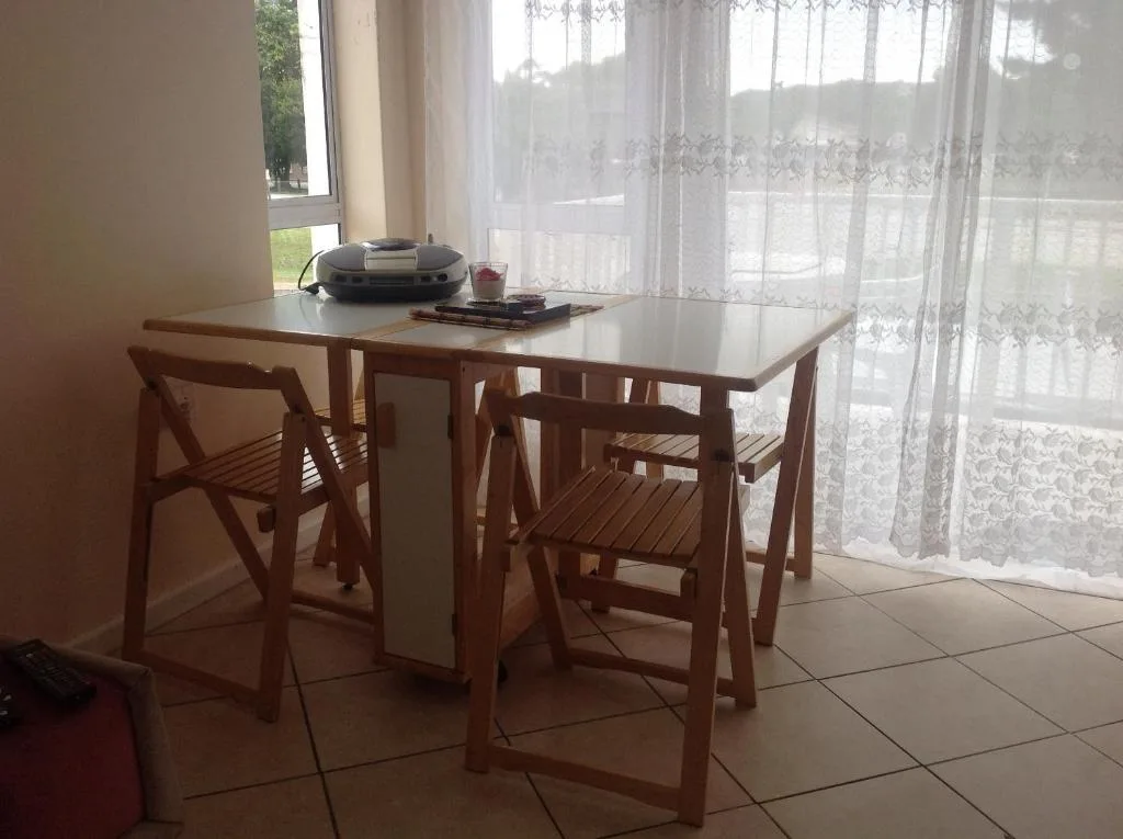 Wooden dining table with chairs near sheer curtained windows overlooking garden