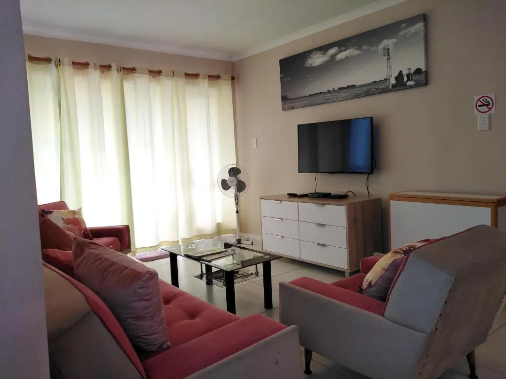 Bright living room with red sofas, wall-mounted TV, and large windows