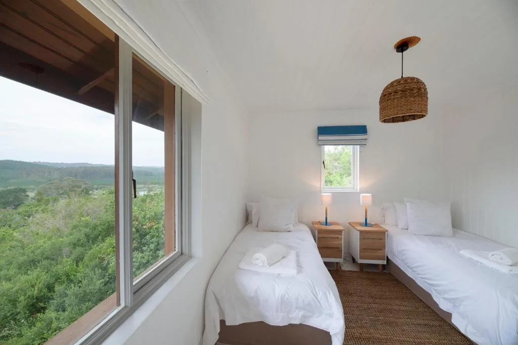 Twin bedroom with white bedding, wooden nightstands, and panoramic garden views