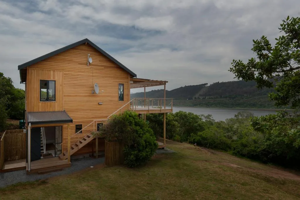 Modern wooden cabin with deck overlooking lagoon and forested hills