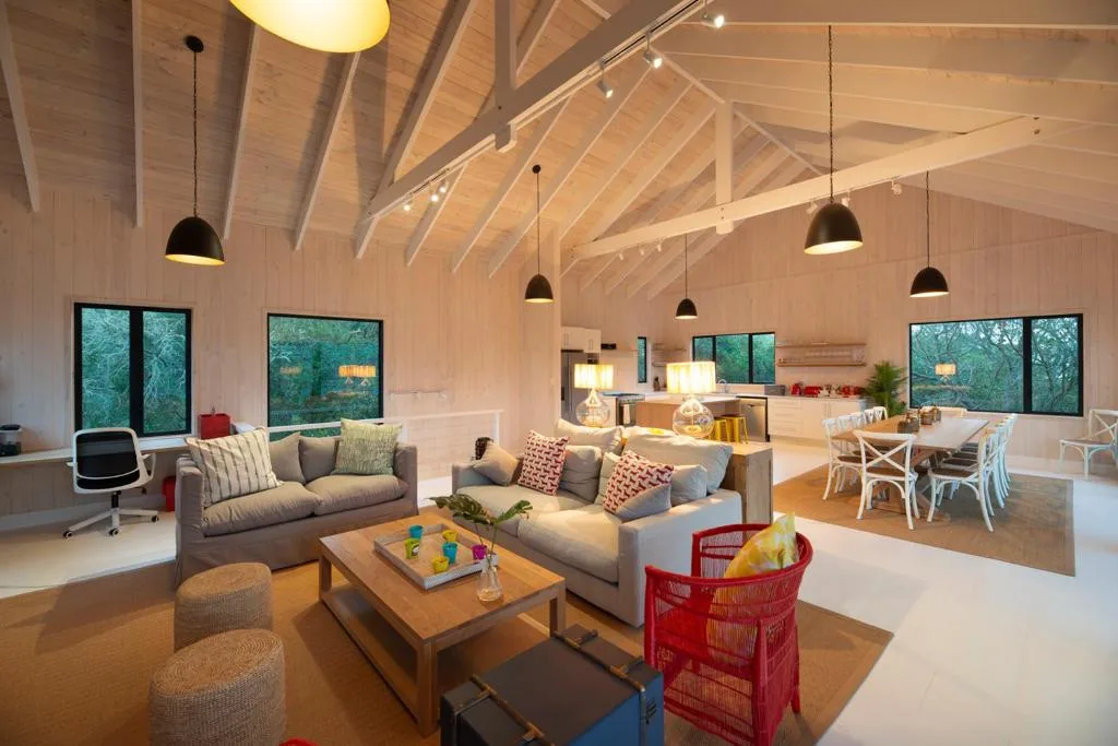 Modern lounge with vaulted ceilings, sofas, and pendant lighting overlooking garden