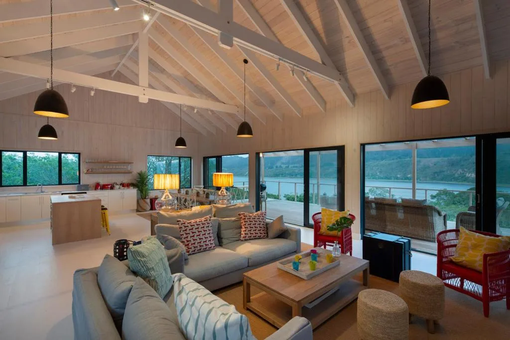 Modern open-plan lounge with sofa, lagoon views through large windows, pendant lighting