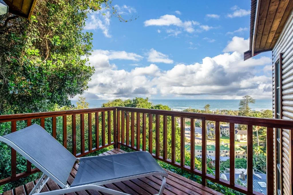 Wooden deck with ocean view, lounge chair, lush greenery, coastal horizon