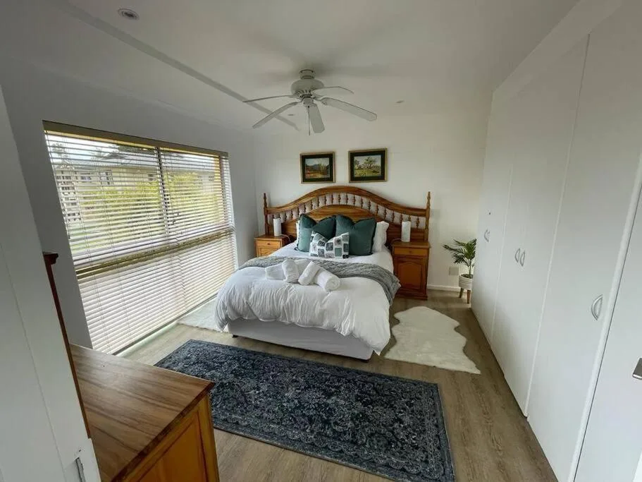 Bright bedroom with wooden bed frame, white bedding, and large shuttered window