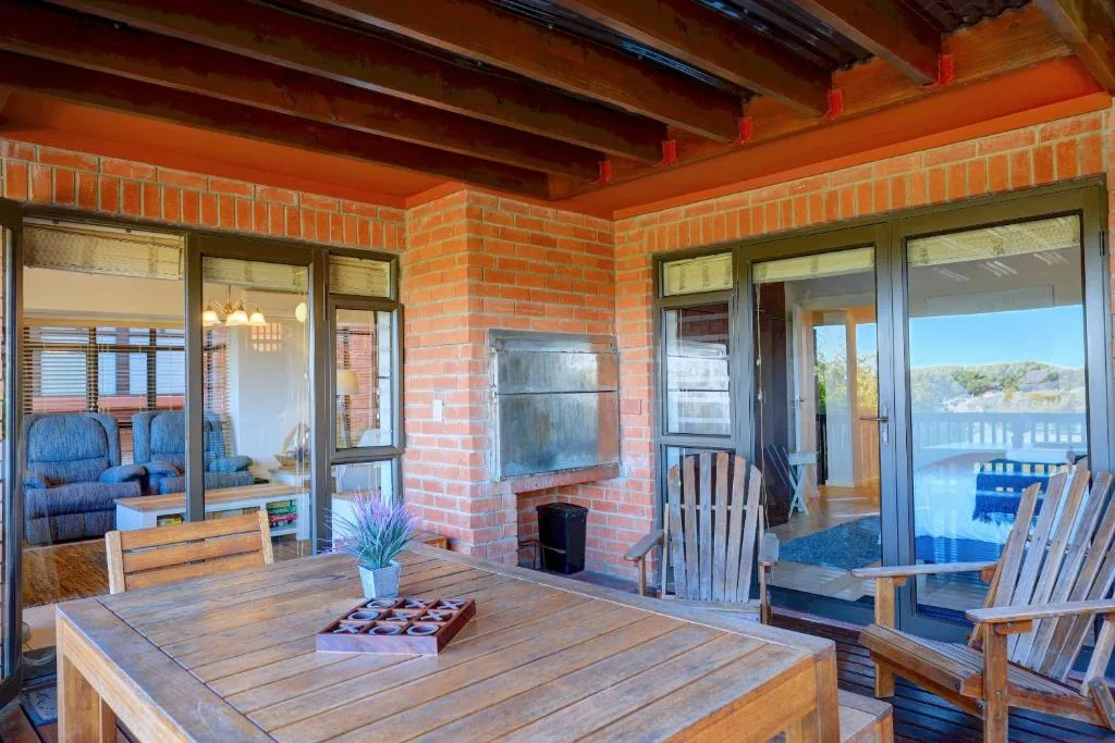 Spacious wooden deck with dining table and Adirondack chairs overlooking water
