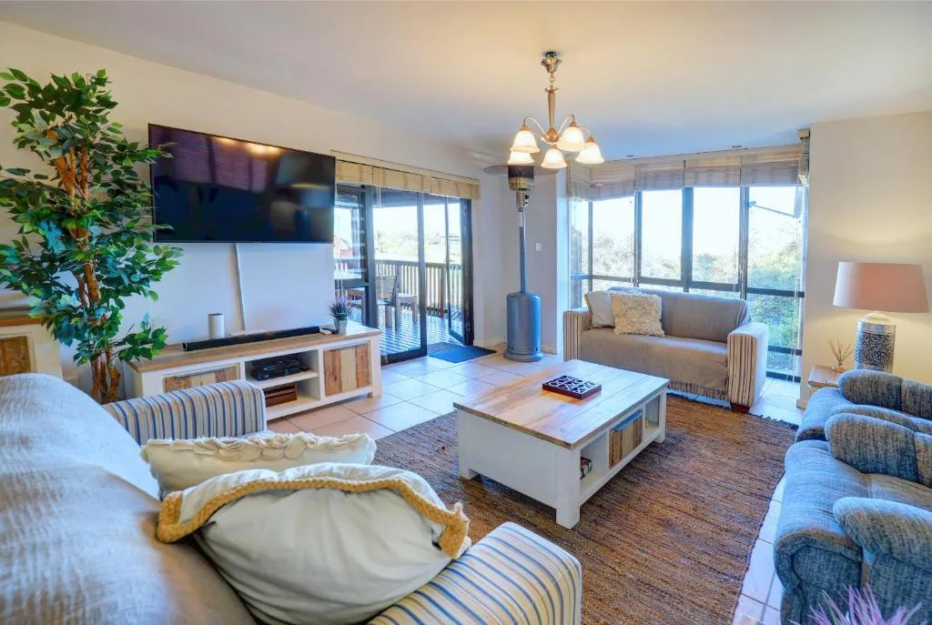 Bright living room with sofas, TV, coffee table, and garden views through doors
