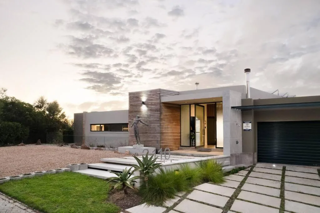 Modern contemporary house with wooden entrance, manicured gardens, dramatic sky