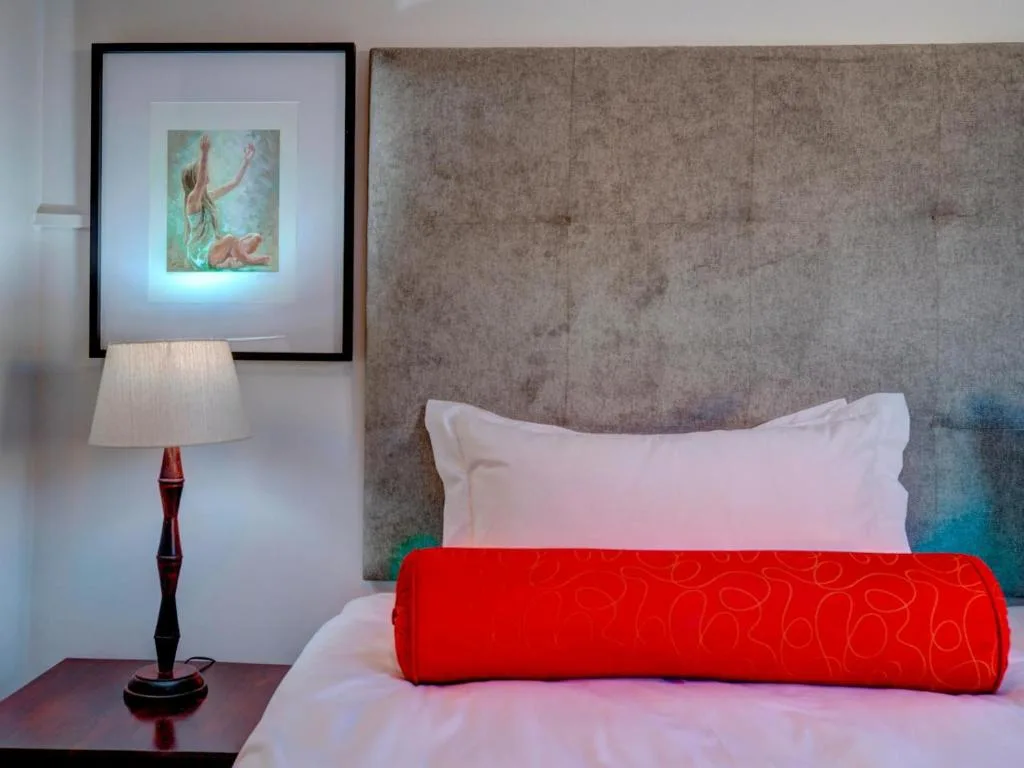 Modern bedroom with upholstered headboard, white pillows, red throw blanket, and bedside lamp