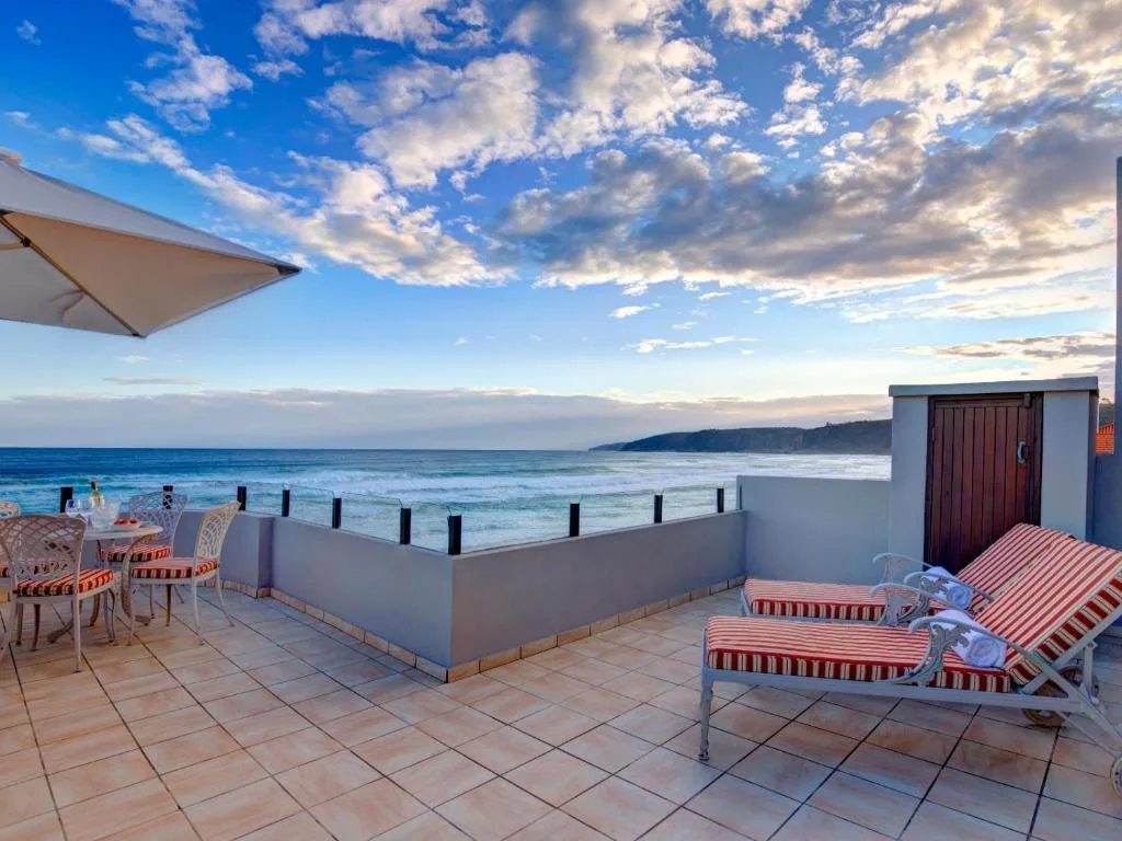 Beachfront deck with loungers overlooking ocean and distant cliffs