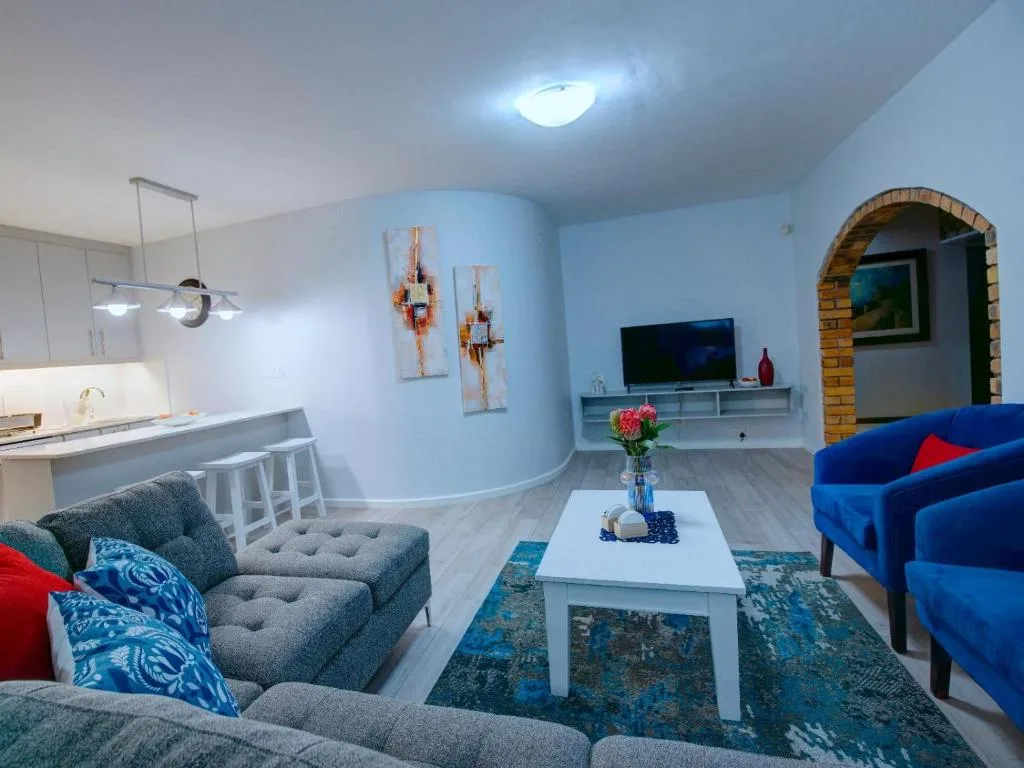 Modern lounge with blue sofas, gray armchair, white coffee table, and open-plan kitchen