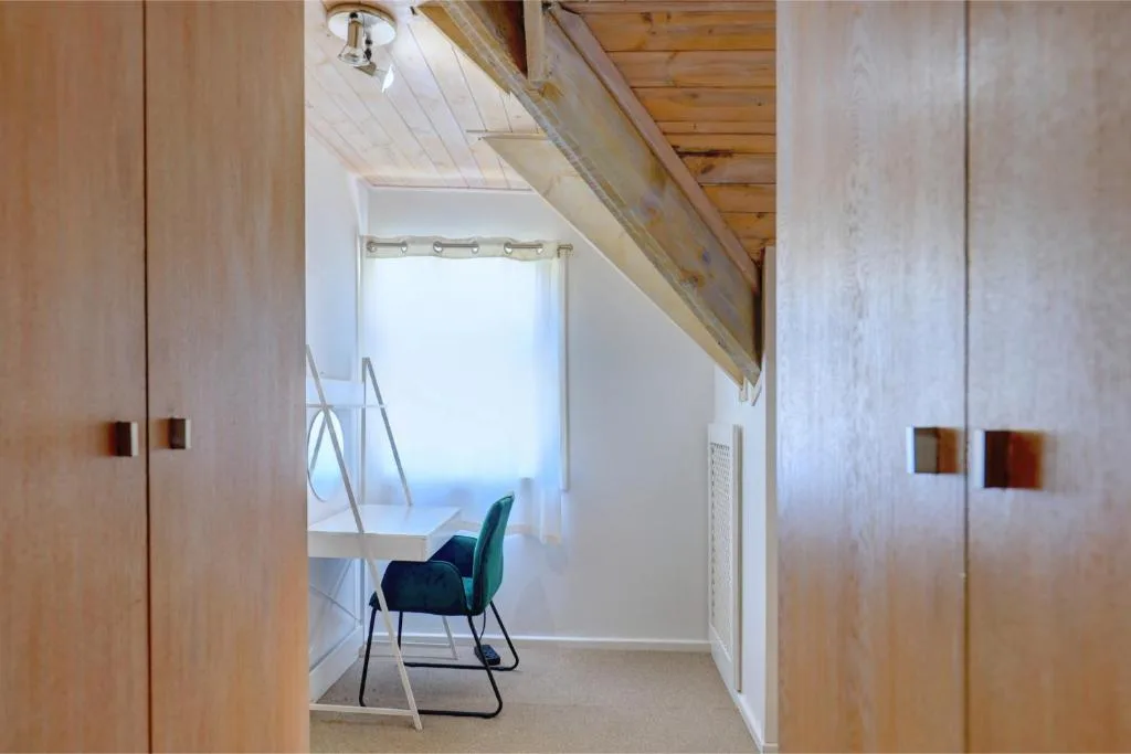 Bright bedroom with wooden beams, built-in cupboards, chair by window