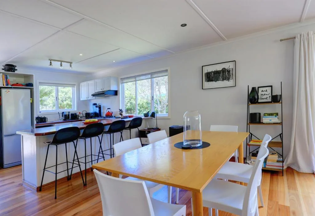 Modern dining room with wooden table and white chairs overlooking kitchen