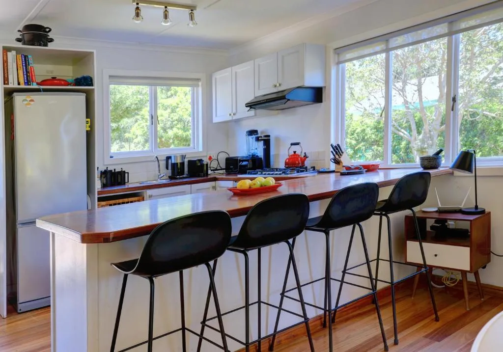 Modern kitchen with island seating, white cabinetry, and garden views through large windows