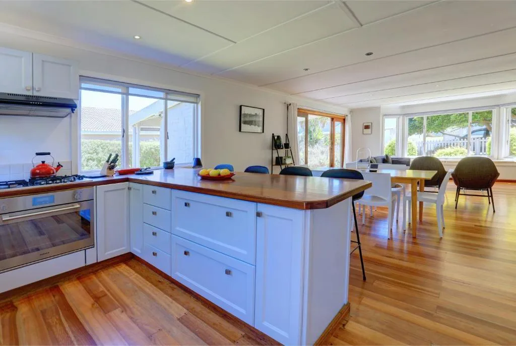 Modern white kitchen with island, wooden countertop, and garden views