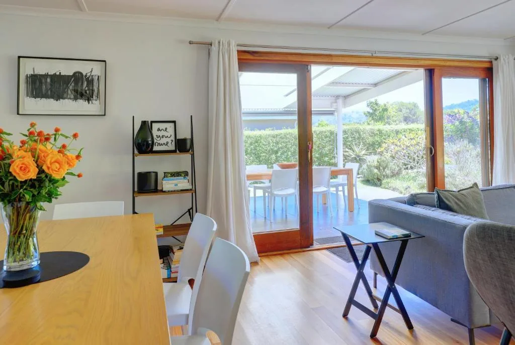 Open-plan living area with sofa, dining table, and scenic garden views through glass doors