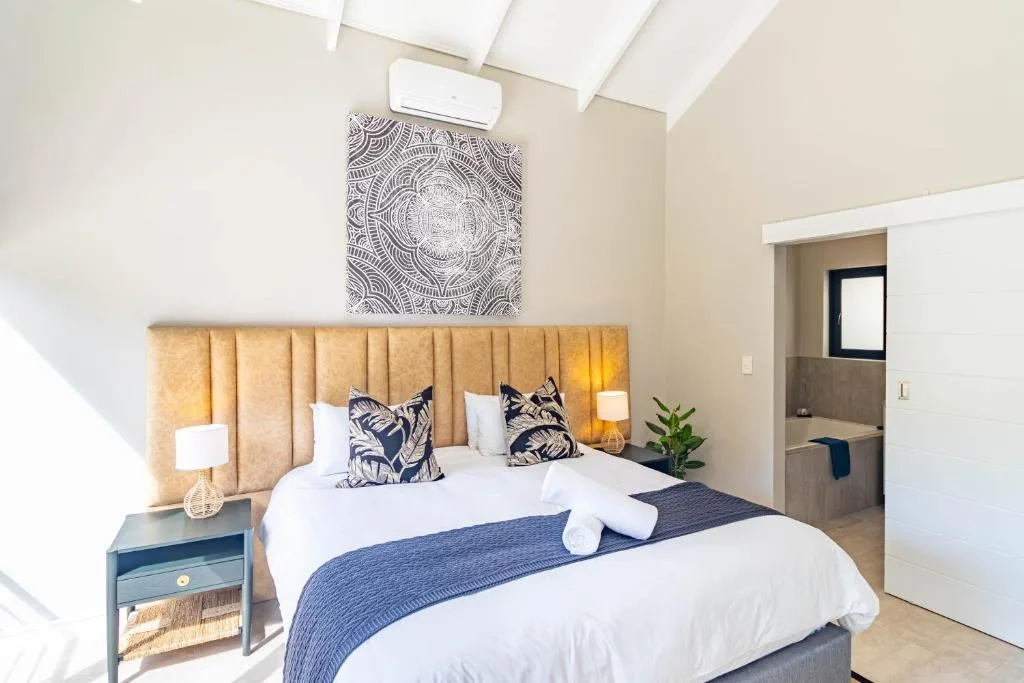 Bright bedroom with golden headboard, white bedding, and ensuite bathroom visible
