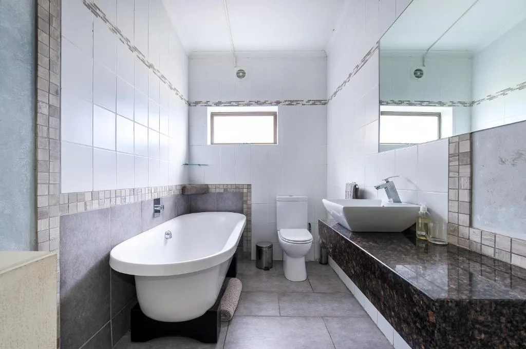 Modern bathroom with freestanding bathtub, toilet, and granite countertop sink