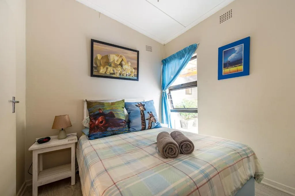 Bright bedroom with queen bed, colorful pillows, rolled towels, and coastal artwork
