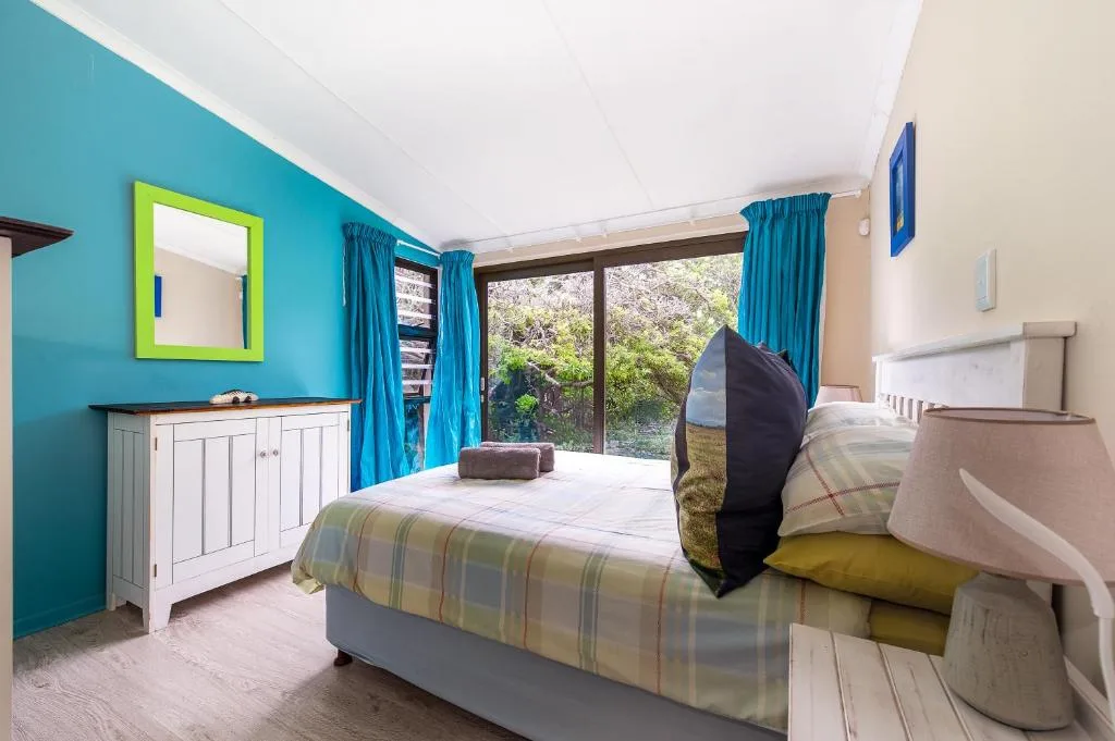 Bright bedroom with turquoise walls, twin beds, and garden views through sliding doors