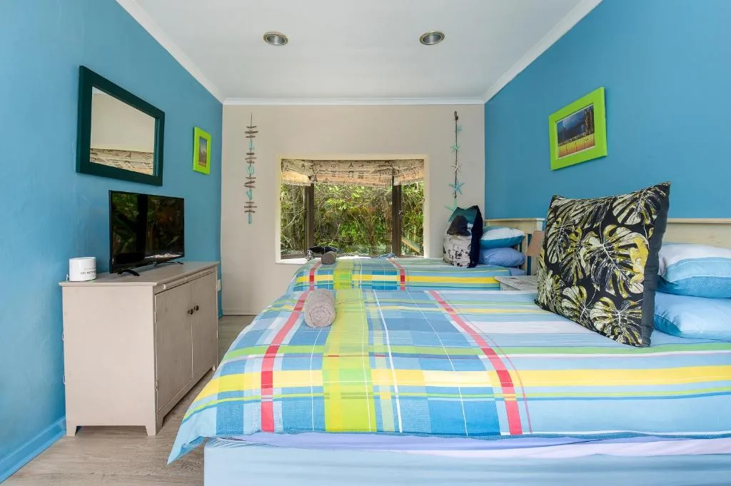 Bright blue bedroom with twin beds and colorful striped bedding, garden views