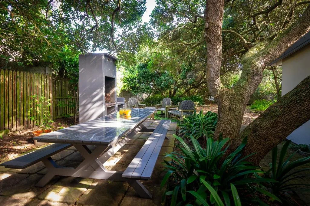 Shaded outdoor braai area with picnic table under mature trees