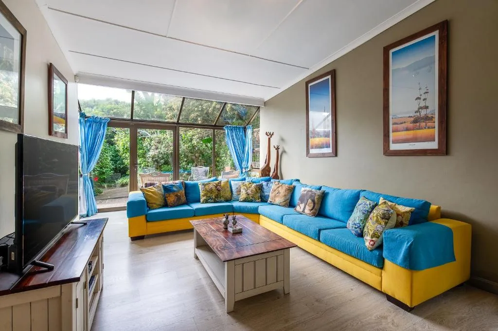 Bright lounge with blue and yellow sectional sofa, TV, and garden views