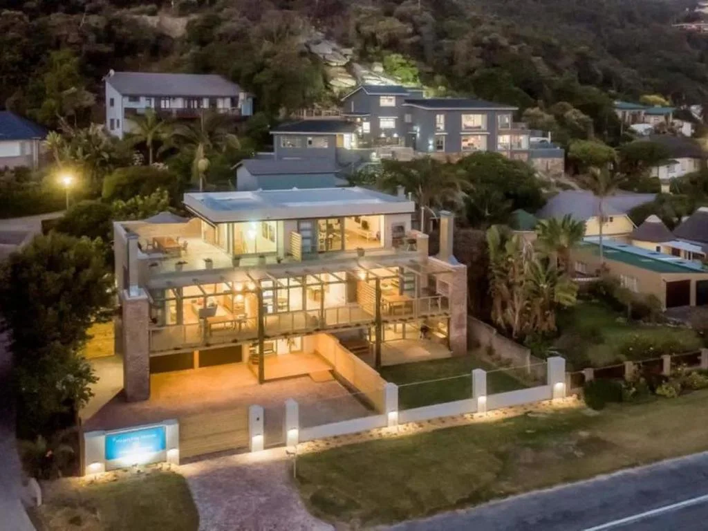 Modern multi-level house with illuminated deck and manicured gardens at dusk