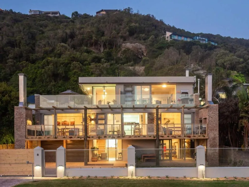 Modern multi-story brick home with glass balconies overlooking forested hillside