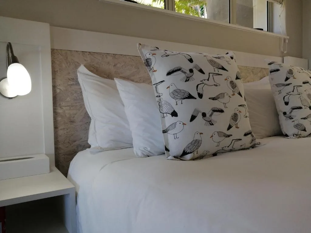 Bed with white linens and bird-patterned decorative pillows, bedside lamp