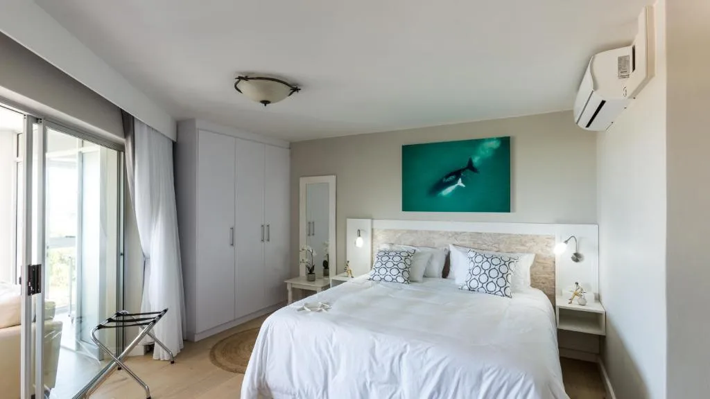 Modern bedroom with white bed, integrated headboard lighting, and ocean artwork