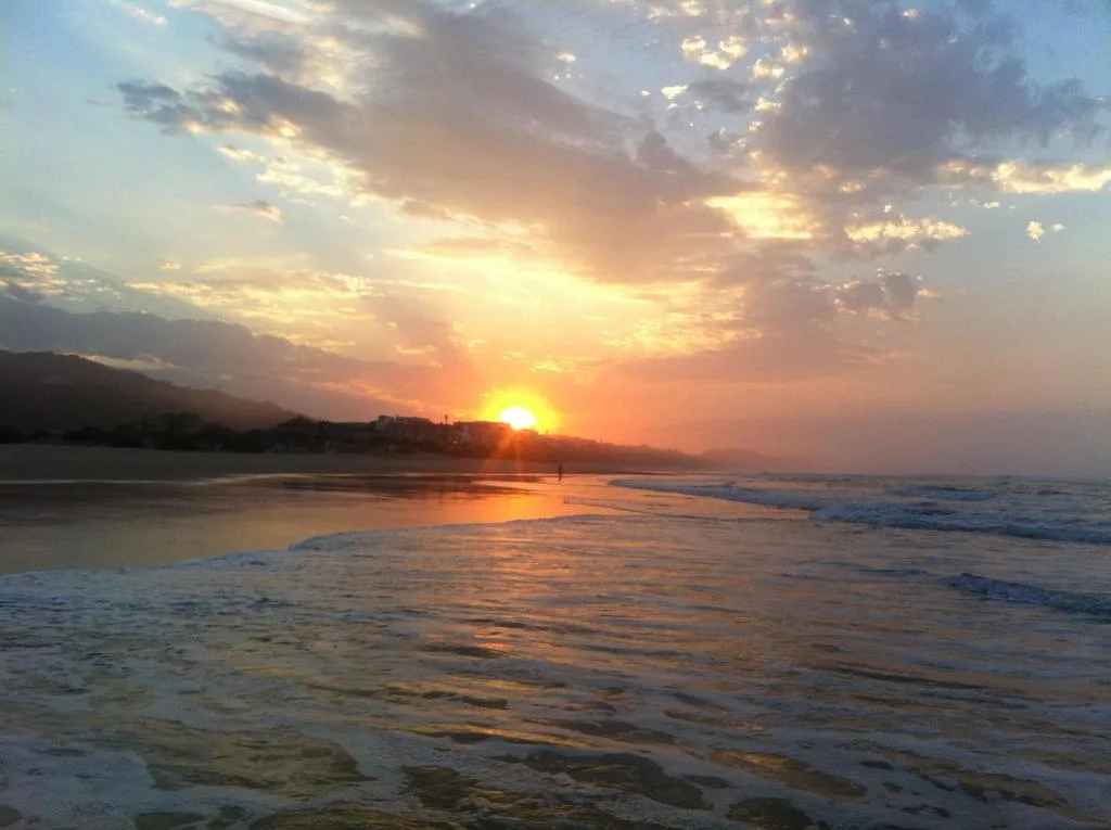 Golden sunset over beach with mountains and ocean waves reflecting light