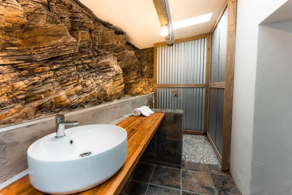 Modern bathroom with round white basin, wooden vanity, and natural stone wall