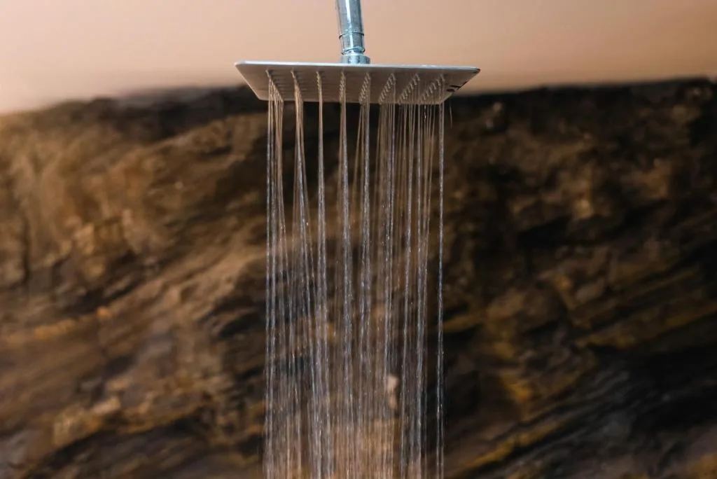 Close-up of rainfall showerhead with water streaming down outdoors