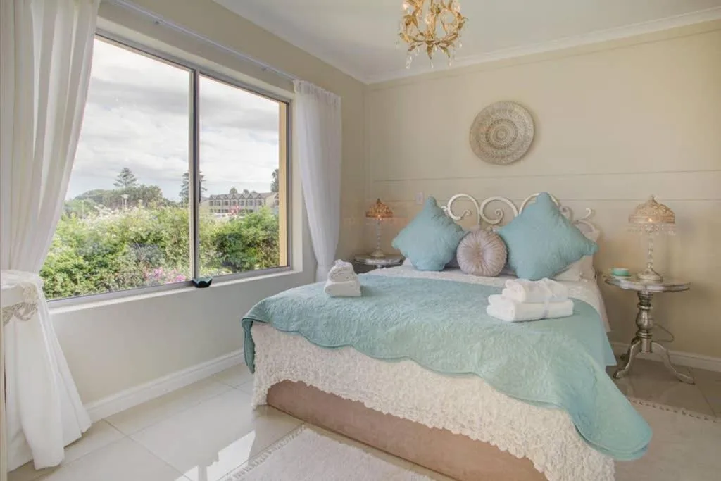 Light-filled bedroom with turquoise bedding, ornate headboard, and large window overlooking gardens