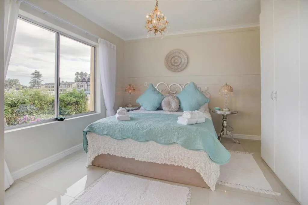 Bright bedroom with turquoise bedding, decorative pillows, and large windows overlooking garden