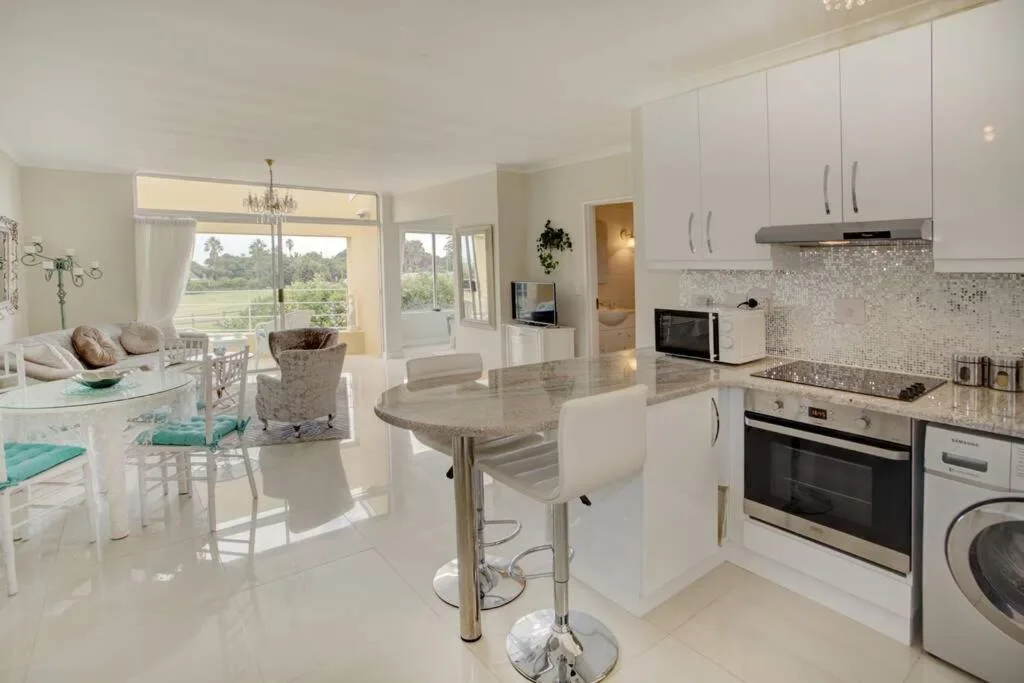Modern white kitchen with island, stainless steel appliances, and garden views
