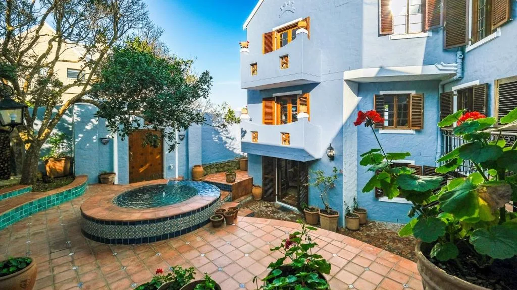 Blue and white villa exterior with courtyard, fountain, and flowering plants