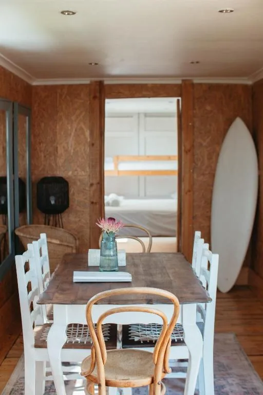 Dining room with wooden table, white chairs, and surfboard decor