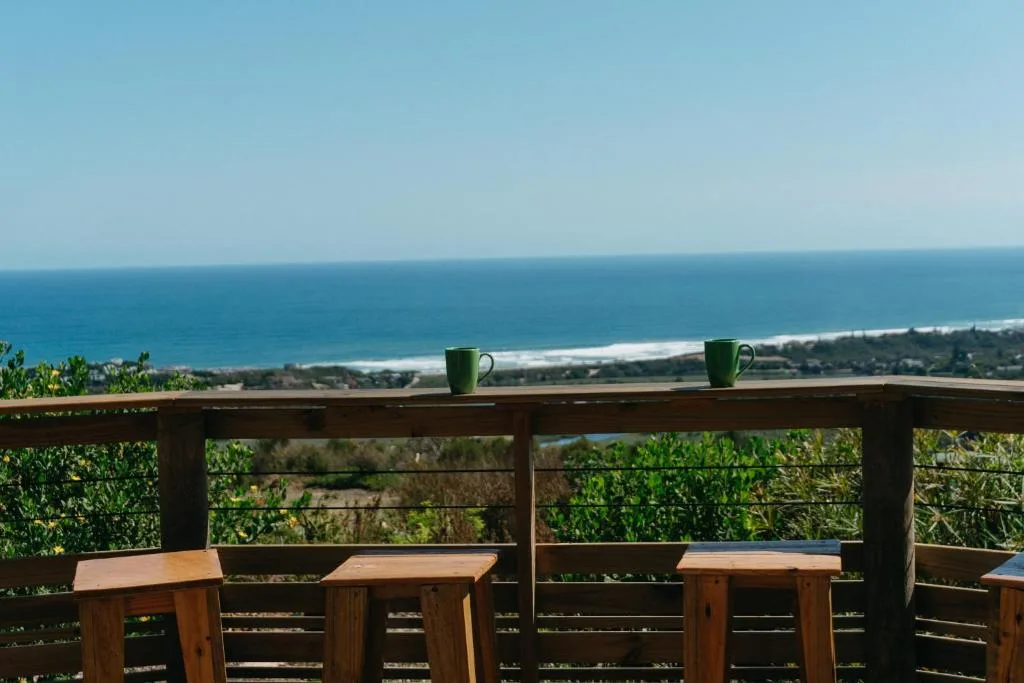 Ocean and coastal landscape visible from wooden deck with coffee cups