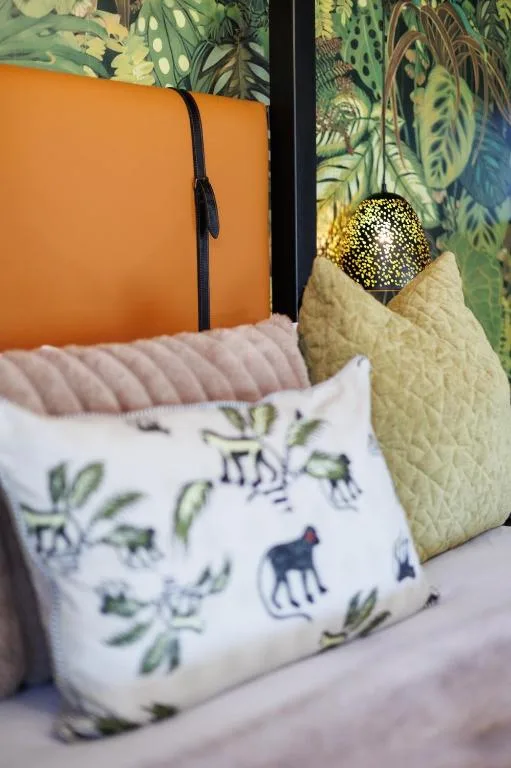 Colorful decorative pillows on a bed with tropical plant backdrop