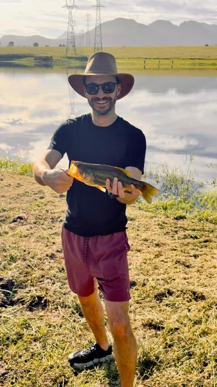 Man holding fish with mountains and river landscape behind him