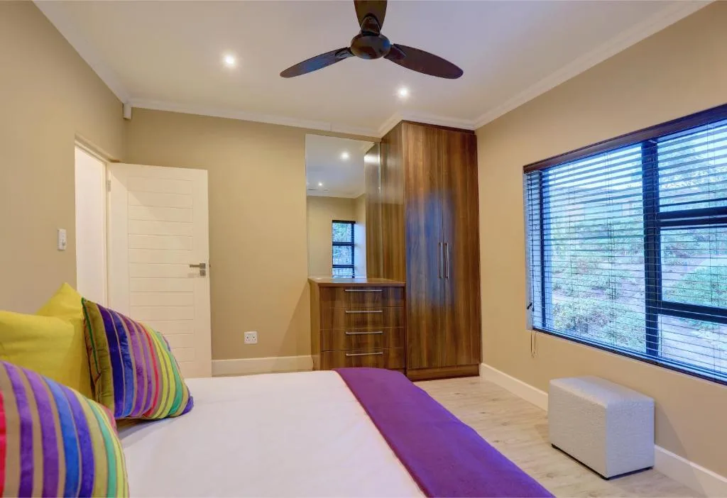 Bright bedroom with colorful pillows, wooden wardrobes, and ceiling fan