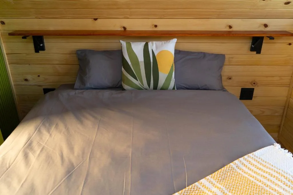 Wooden bedroom with made bed, grey bedding, decorative pillows, natural light