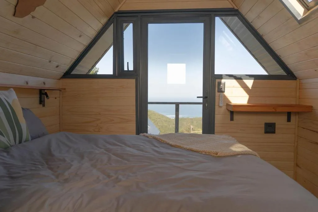Modern bedroom with wooden walls, bed, and panoramic water views through glass doors