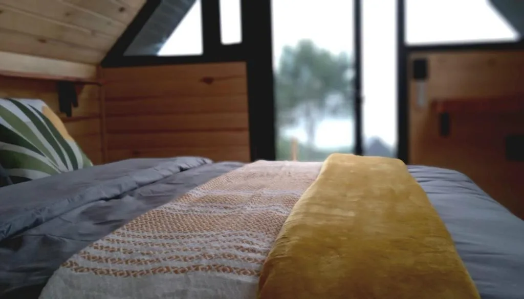 Bed with yellow throw in bright modern bedroom with wood paneling and view