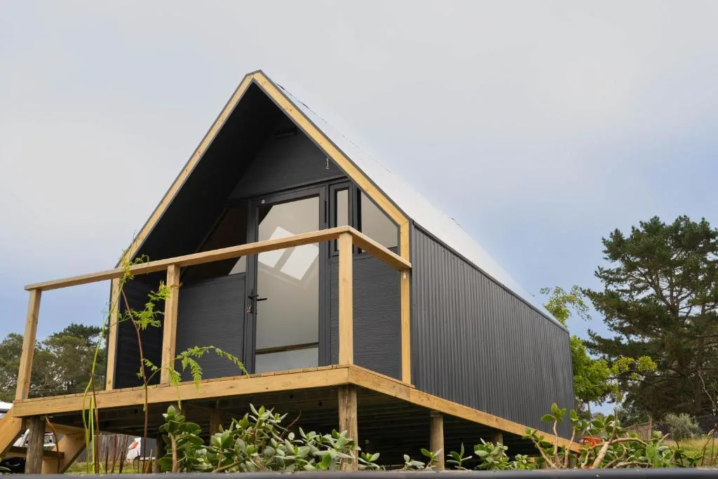 Modern A-frame glamping pod with wooden deck and black metal cladding