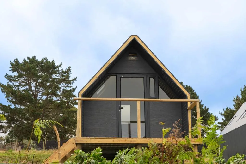 Modern black A-frame glamping cabin with wooden deck and large windows