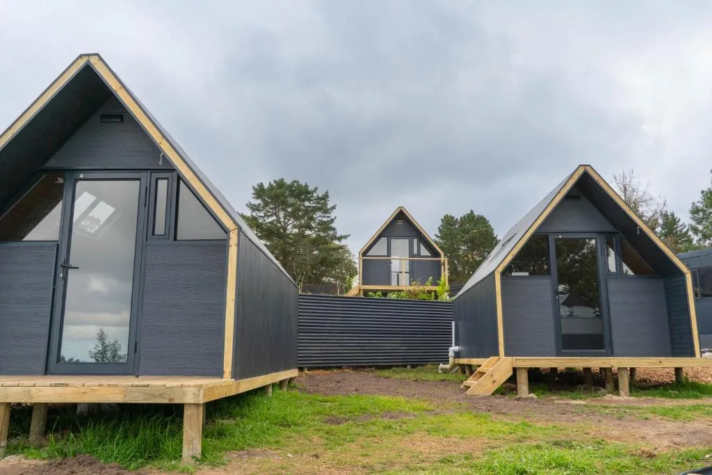 Modern A-frame glamping pods with dark grey cladding and wooden trim